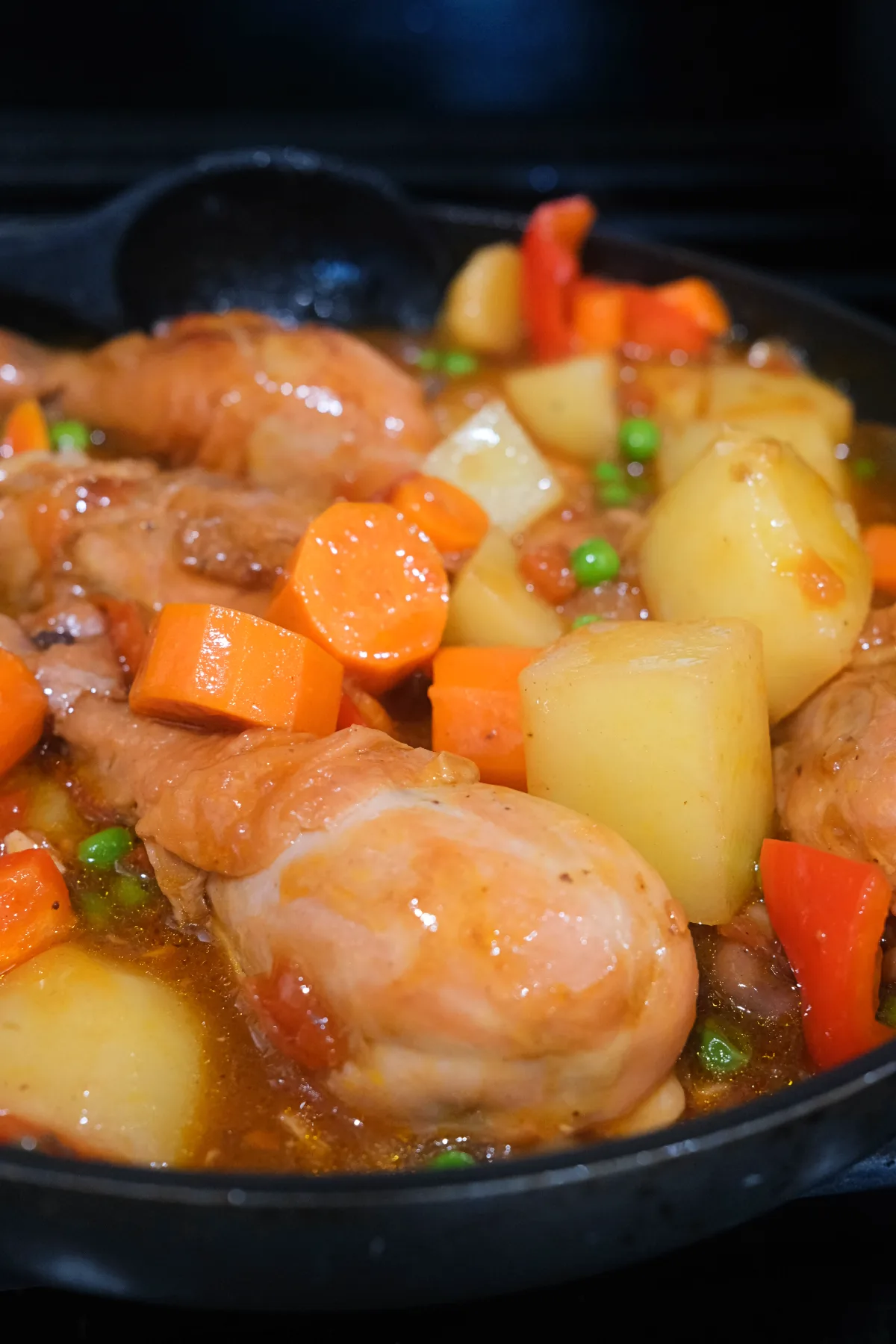 Close-up of Filipino Chicken Afritada simmered with chicken drumsticks, potatoes, carrots, bell peppers, and green peas