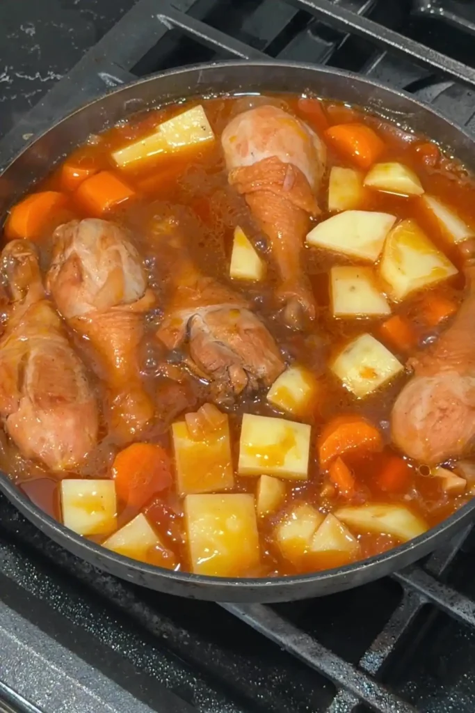 Potatoes and carrots added to simmering chicken afritada for a hearty stew
