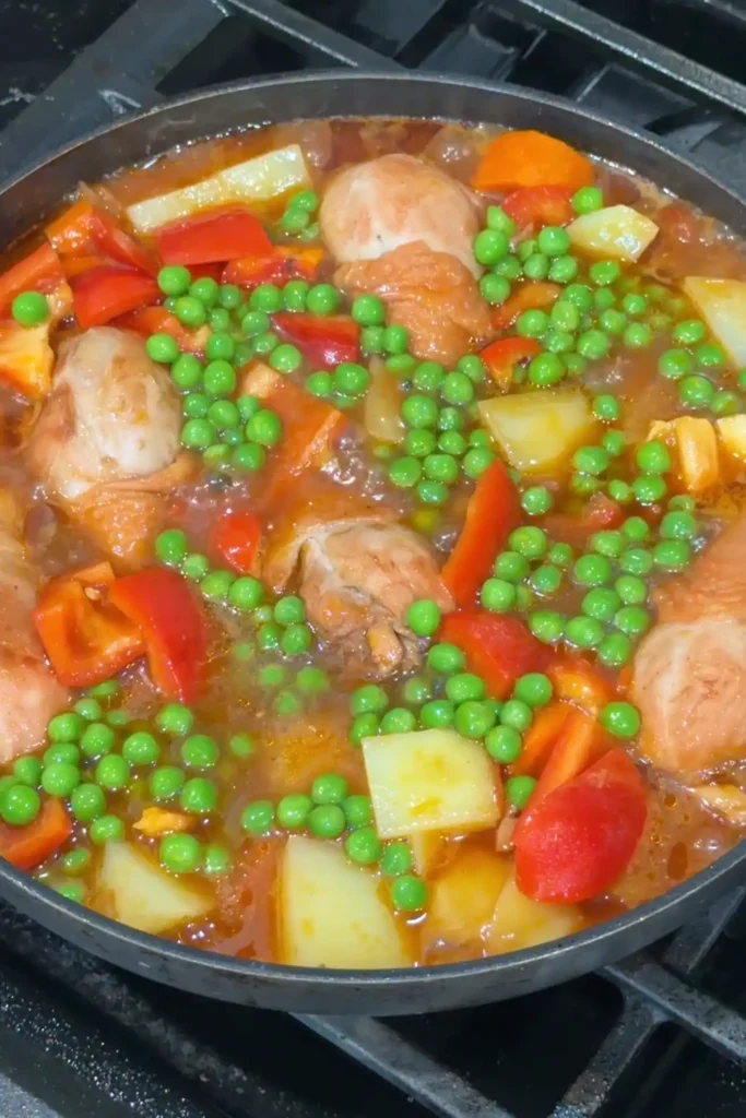 Red bell peppers and green peas added to chicken afritada during the final stage of cooking