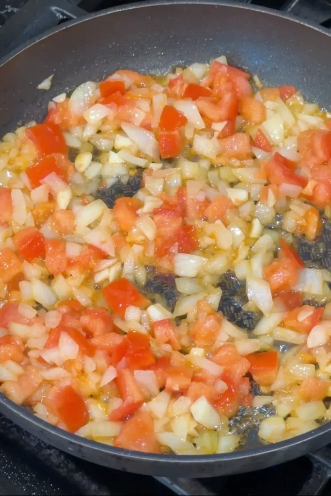 Tomatoes, onions, and garlic cooking until softened for Filipino chicken afritada