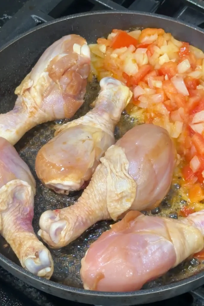 Chicken drumsticks added to sautéed aromatics for homemade chicken afritada
