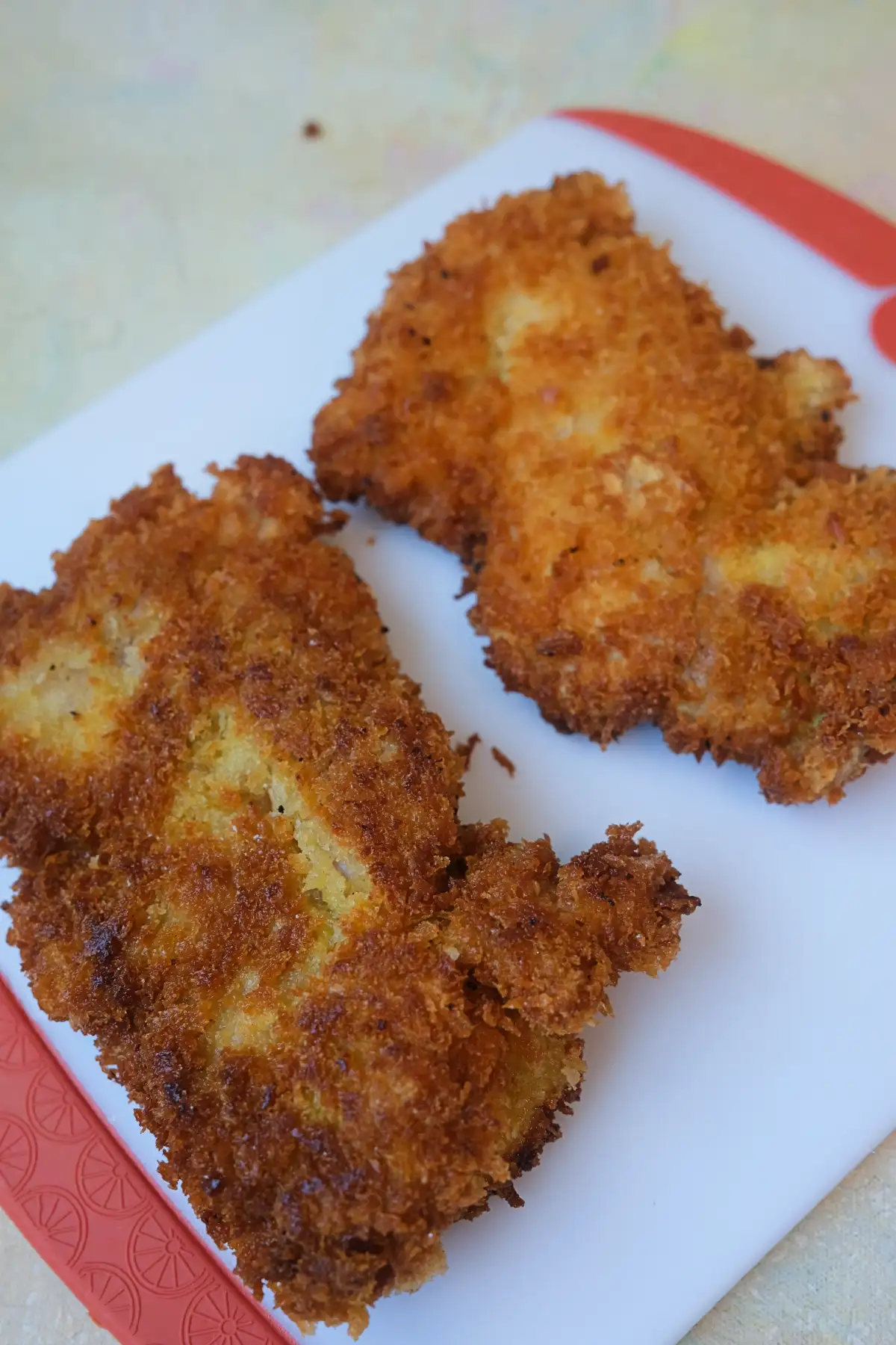 Crispy golden chicken katsu coated in panko breadcrumbs on a cutting board.