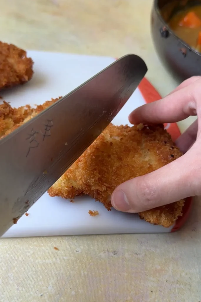 Slicing crispy chicken katsu into strips before serving.