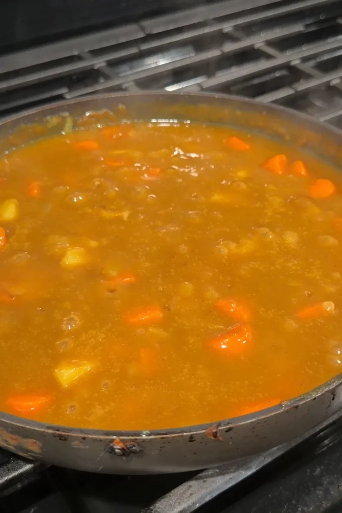 Thick homemade Japanese curry sauce with carrots and potatoes simmering in a pan.