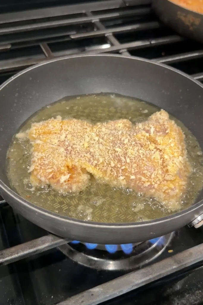 Breaded chicken katsu frying in hot oil until crispy and golden brown.