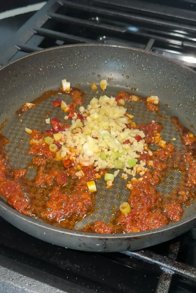 Garlic, ginger, green onions, and chilies cooking with doubanjiang for mapo tofu.