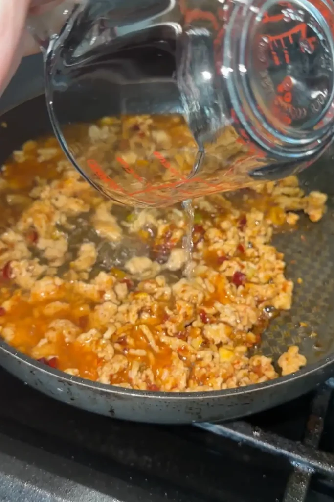 Chicken stock being poured into seasoned ground chicken for mapo tofu sauce.