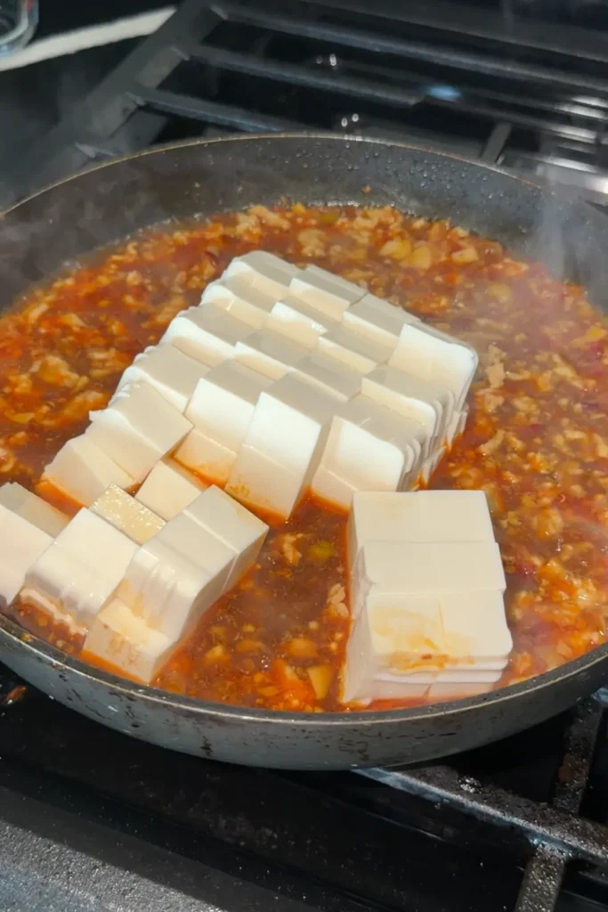 Silken tofu cubes added to spicy chicken mapo tofu sauce.