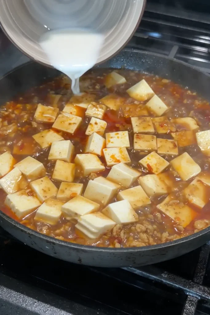 Cornstarch slurry being added to thicken chicken mapo tofu sauce.
