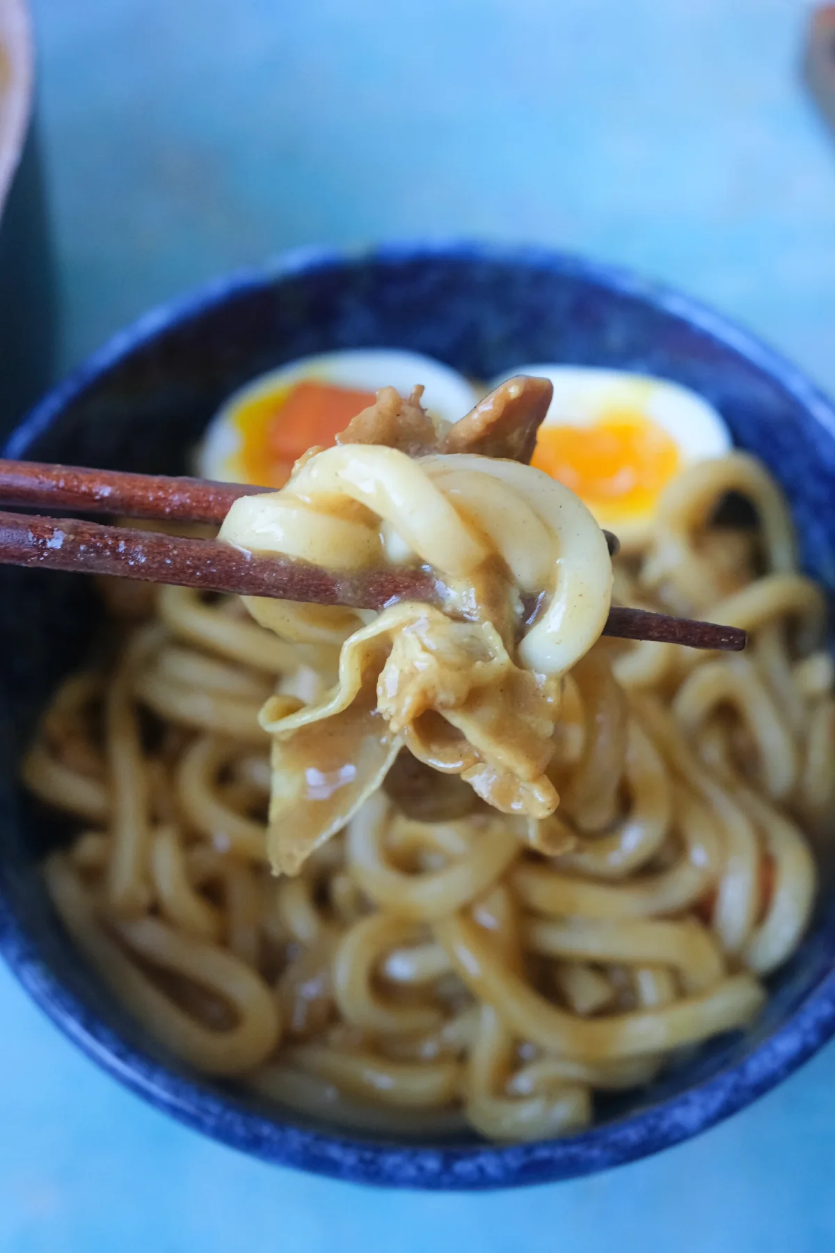 Chewy udon noodles and tender pork belly coated in thick Japanese curry sauce picked up with chopsticks.