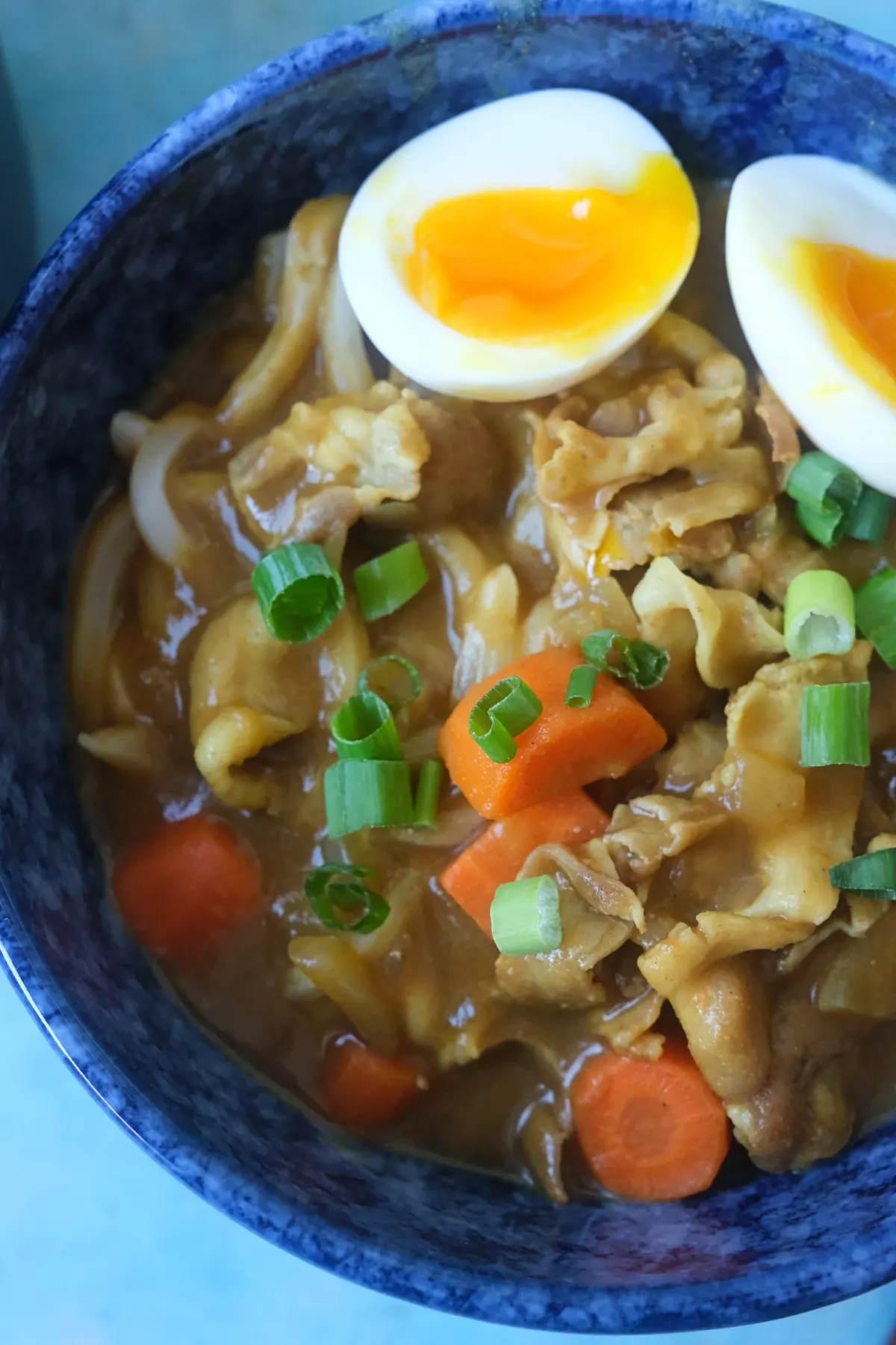 Close-up of Japanese curry udon with pork belly, carrots, green onions, and jammy soft-boiled egg.