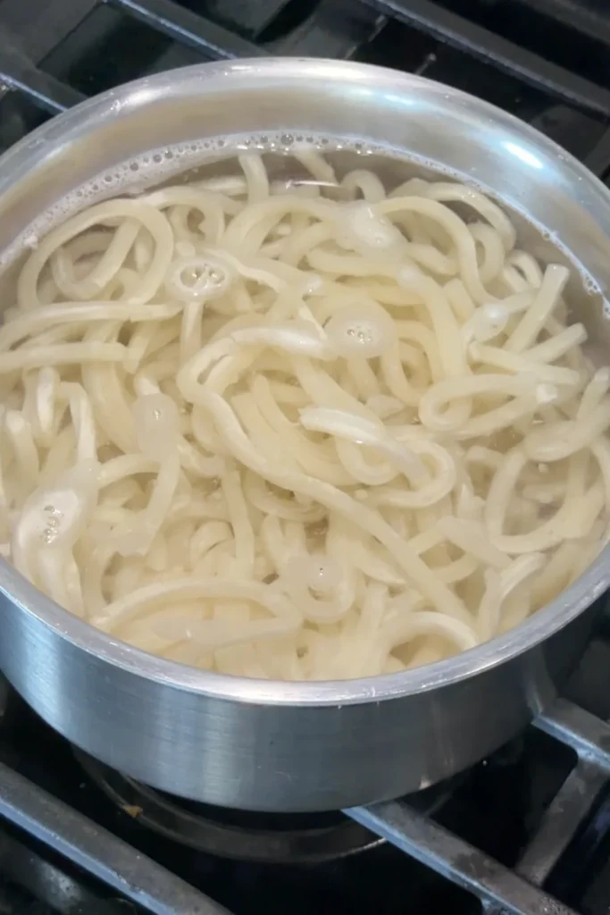 Udon noodles cooking in boiling water until tender and chewy