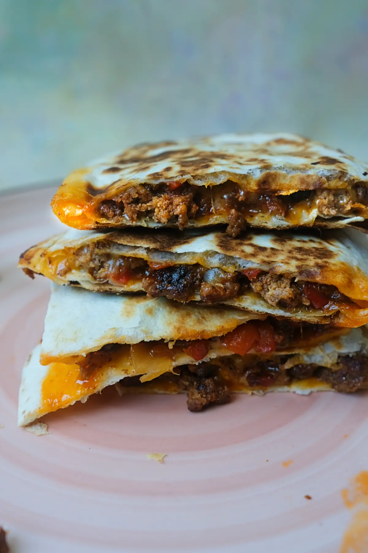 Cheesy ground beef quesadillas stacked on a pink plate with melted cheese and seasoned beef filling visible.
