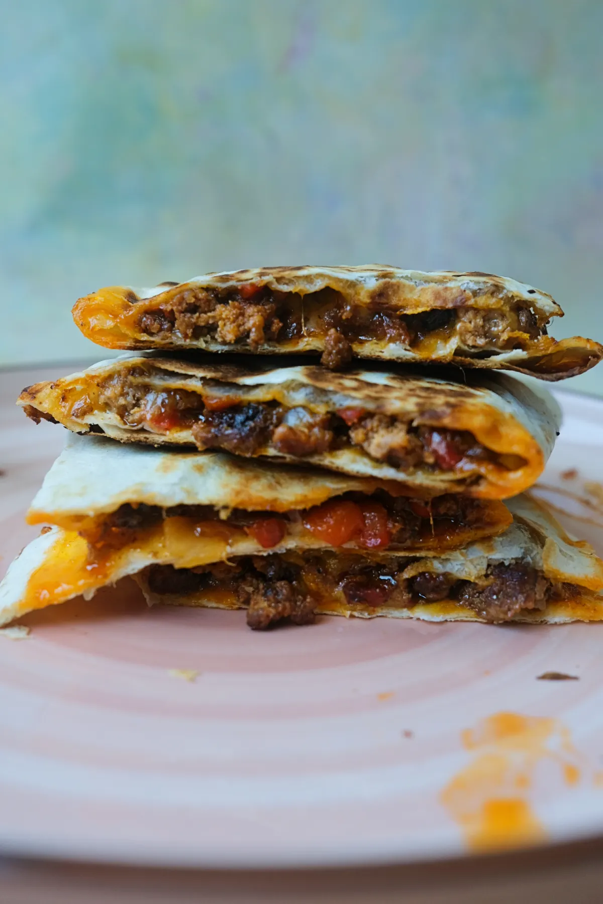 Close-up of cheesy ground beef quesadilla wedges stacked on a plate showing crispy tortillas and savory beef filling.