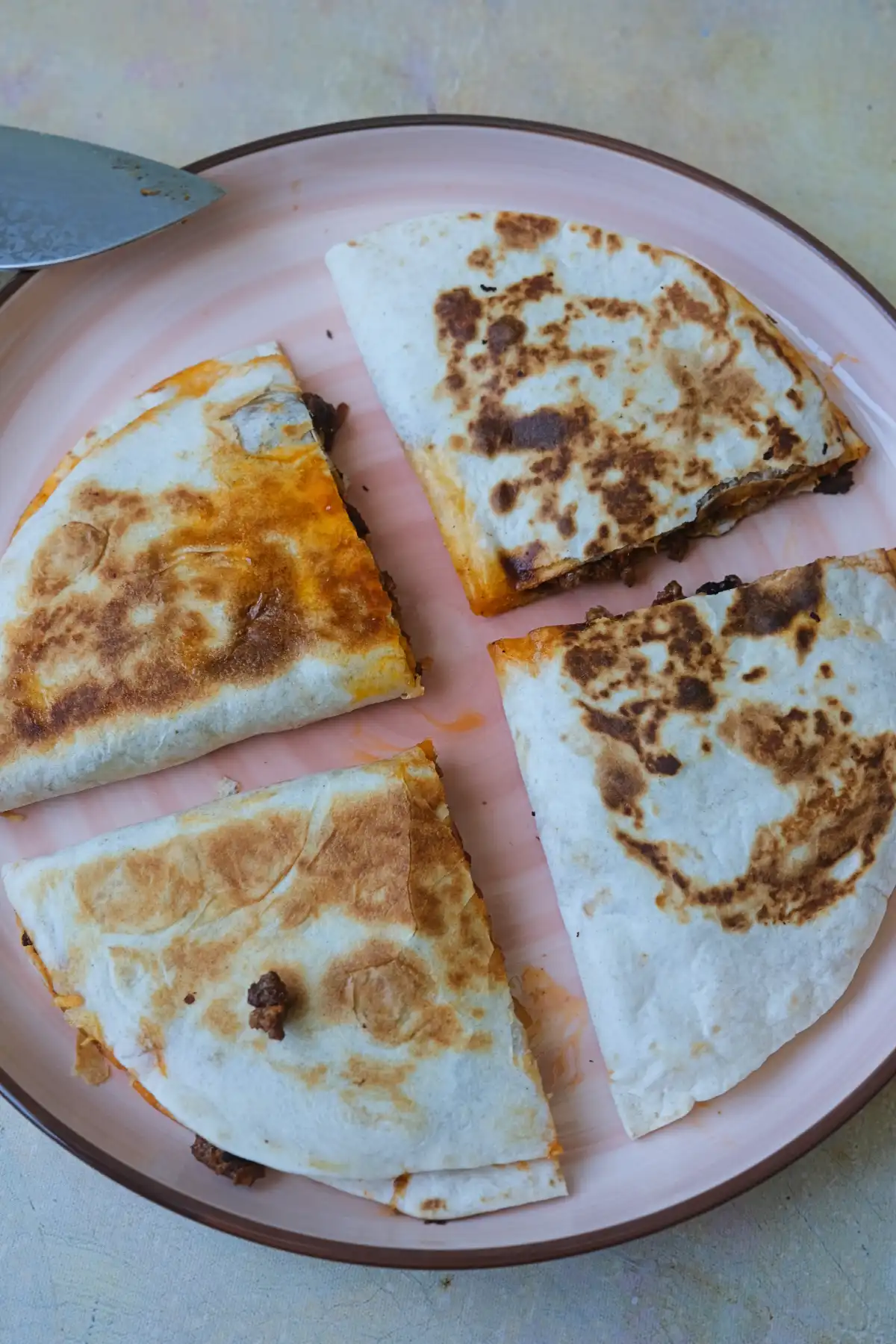 Overhead view of homemade ground beef quesadillas cut into wedges on a pink plate.