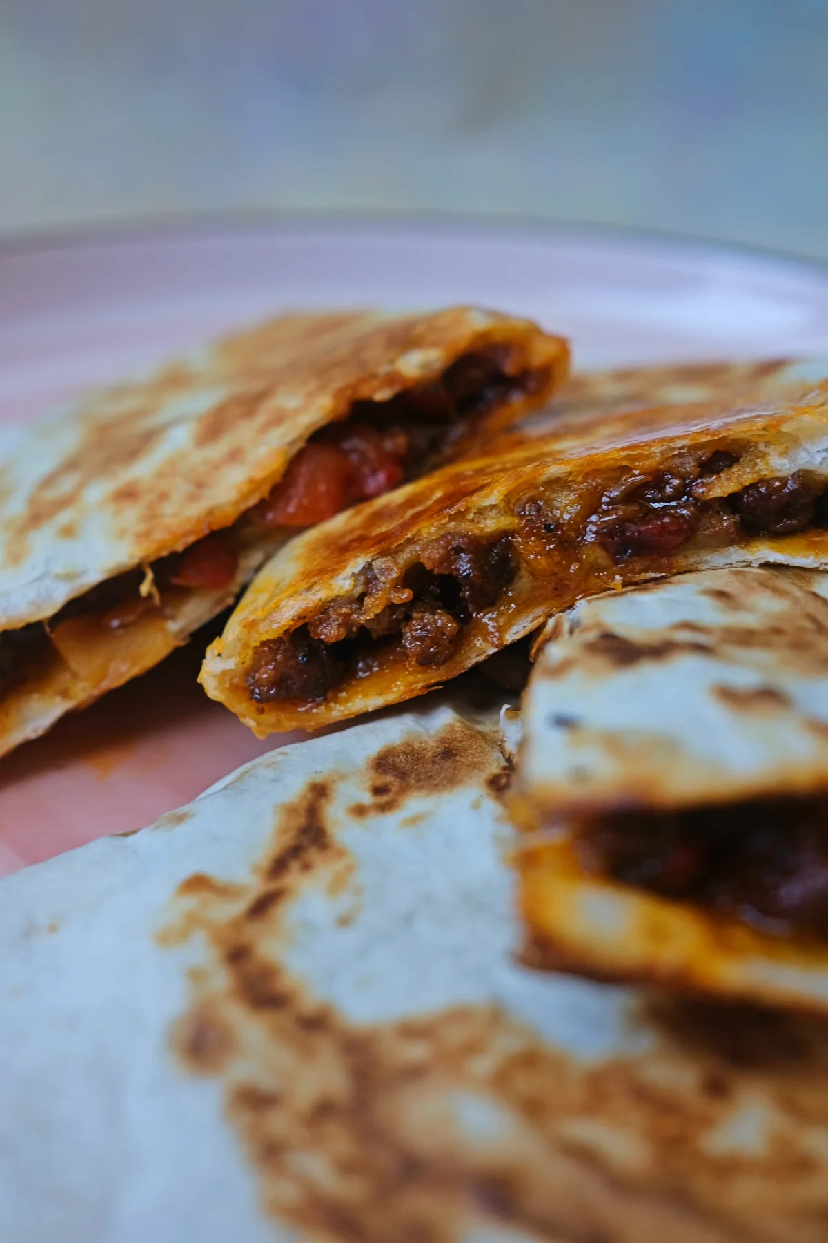 Cheesy beef quesadillas stacked on a plate with golden brown tortillas and gooey melted cheese.