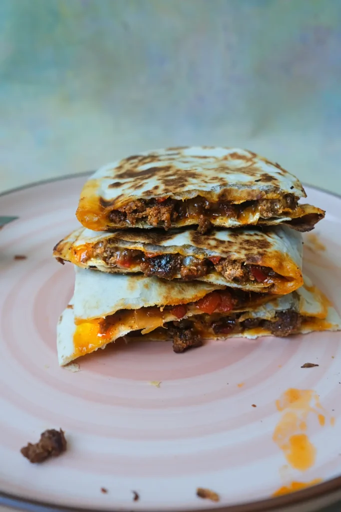 Stacked ground beef quesadilla slices filled with seasoned beef, peppers, onions, and melted cheese on a pink plate.