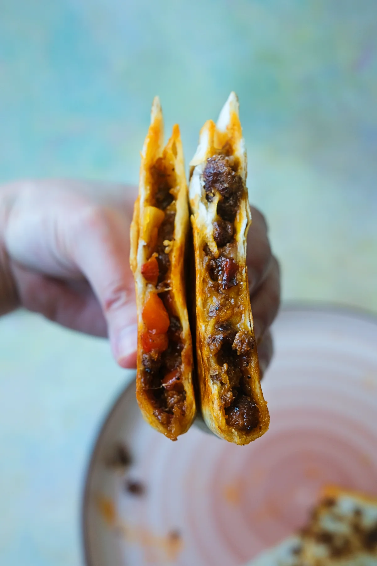 Hand holding two halves of a ground beef quesadilla showing the cheesy seasoned beef filling inside.