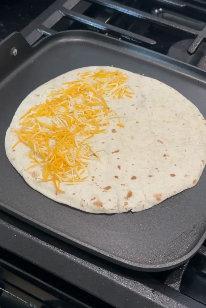 Shredded cheese sprinkled onto a flour tortilla for homemade quesadillas.