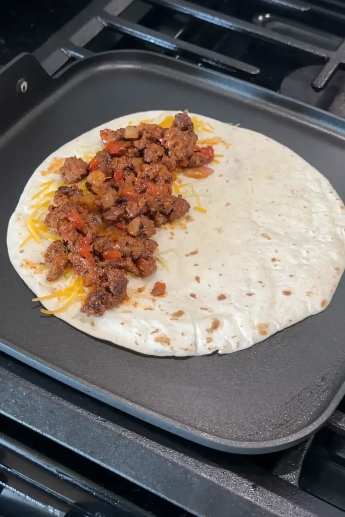 Seasoned ground beef filling layered over cheese on a flour tortilla.