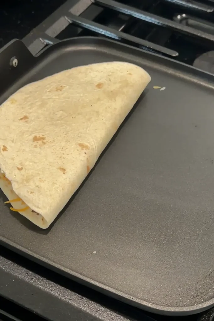 Ground beef quesadilla folded in half and cooking on a griddle.
