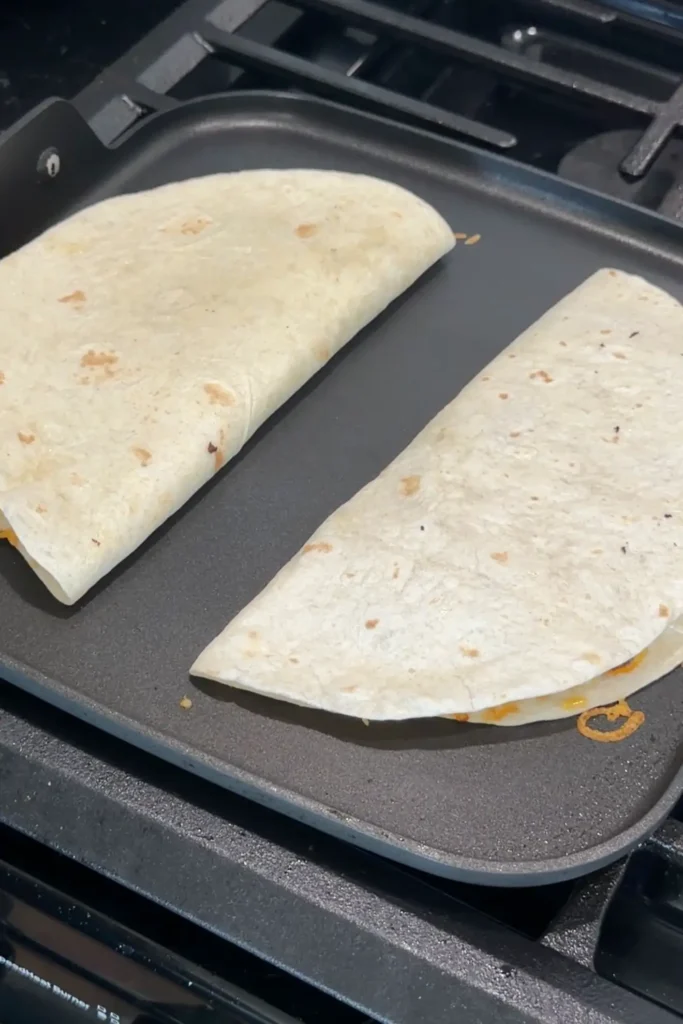 Two folded ground beef quesadillas cooking on a griddle until golden brown.