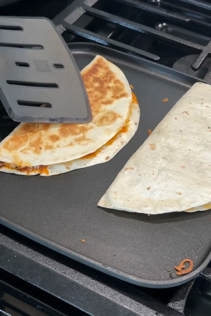 Ground beef quesadilla being pressed with a spatula while cooking until crispy and golden.