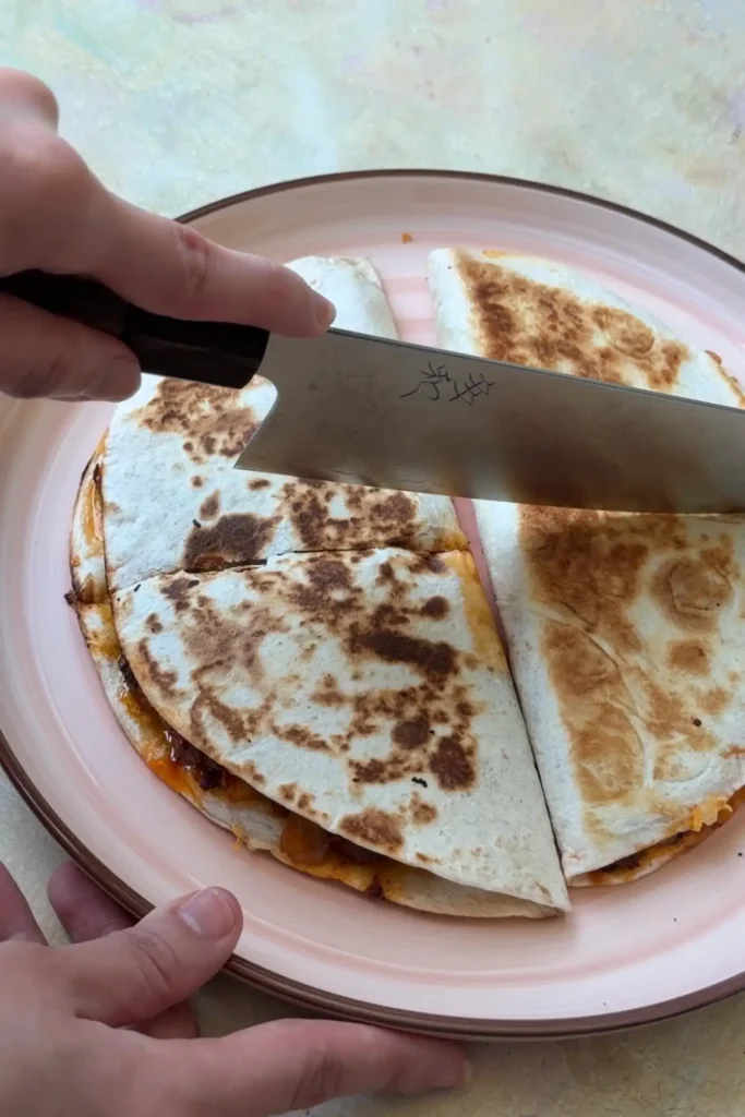 Ground beef quesadilla being sliced into wedges on a pink plate after cooking until golden and crispy.