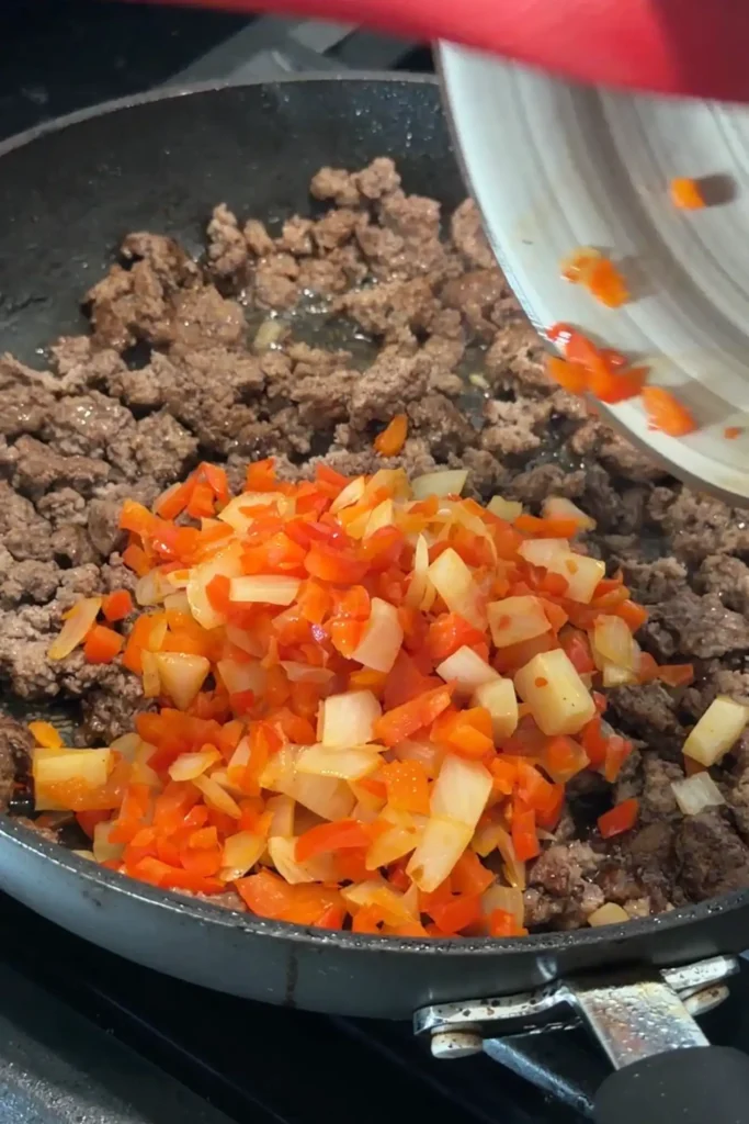 Cooked ground beef topped with sautéed onions and bell peppers in a skillet.