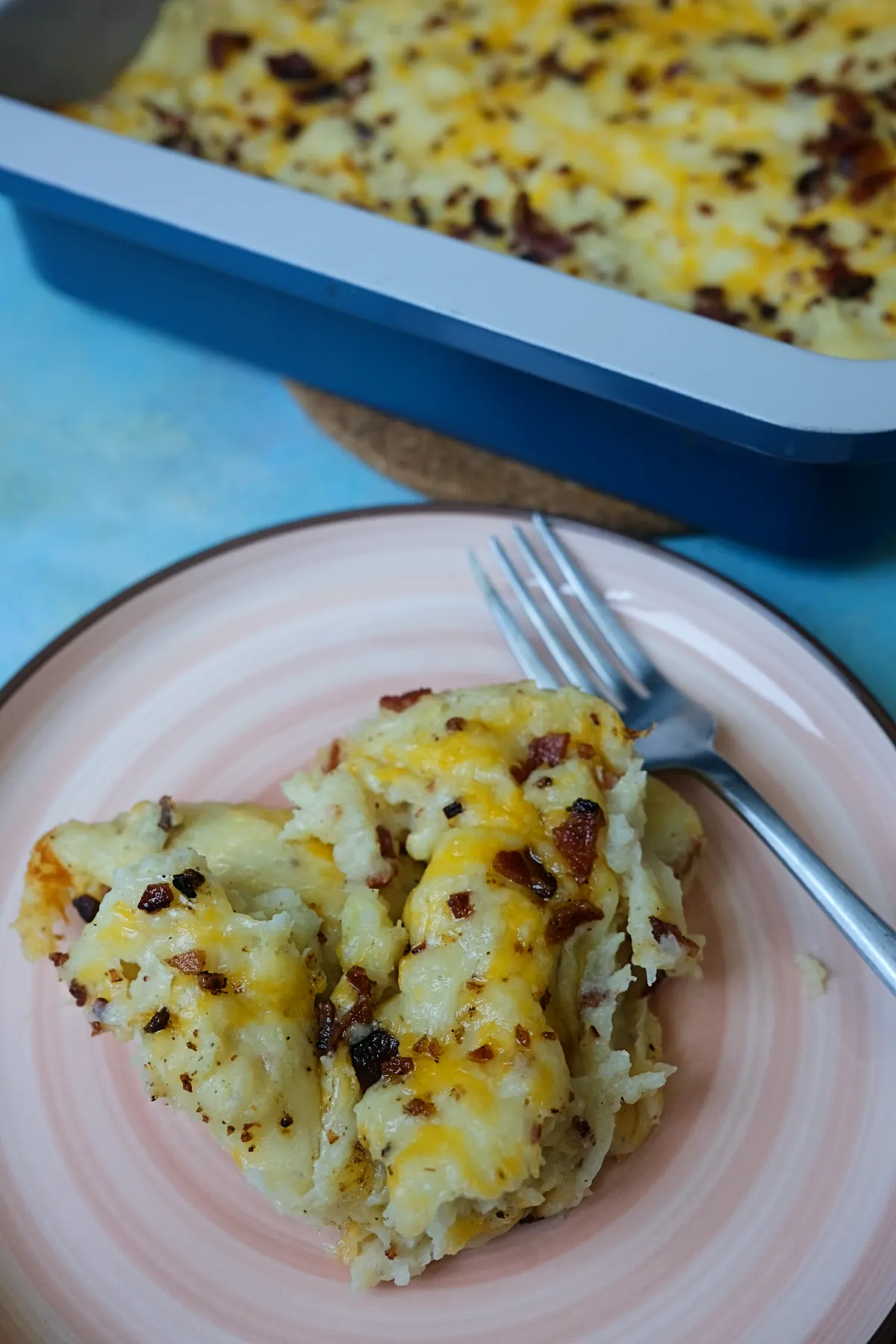 Loaded baked potato casserole served on a pink plate with a baking dish in the background.