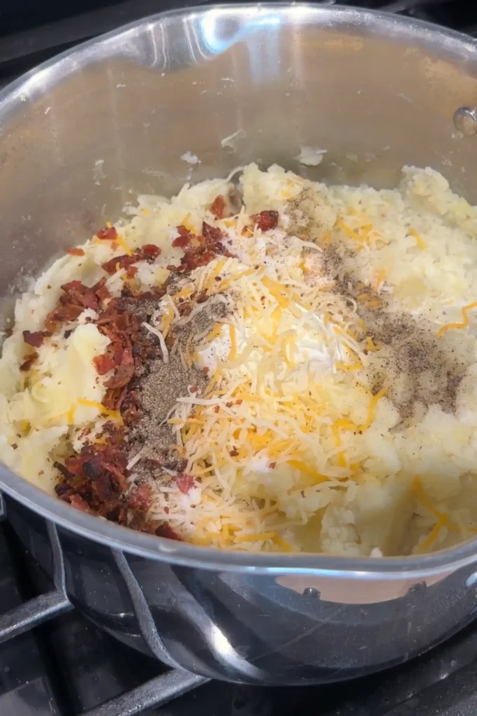 Mashed potatoes mixed with cheese, bacon, salt, and pepper in a pot.