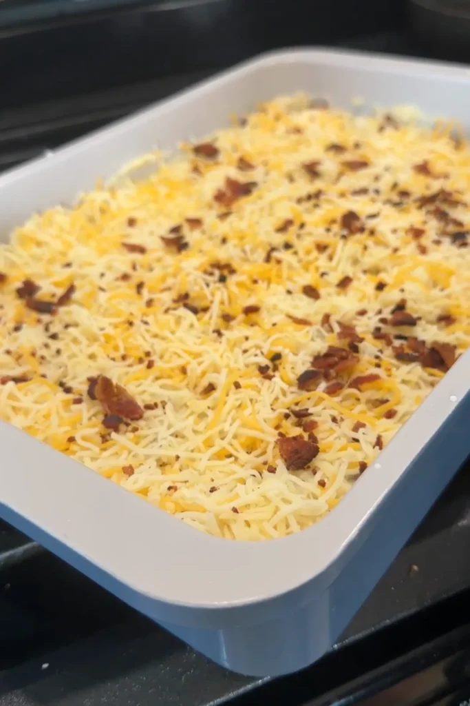 Potato casserole topped with shredded cheese and bacon before baking.