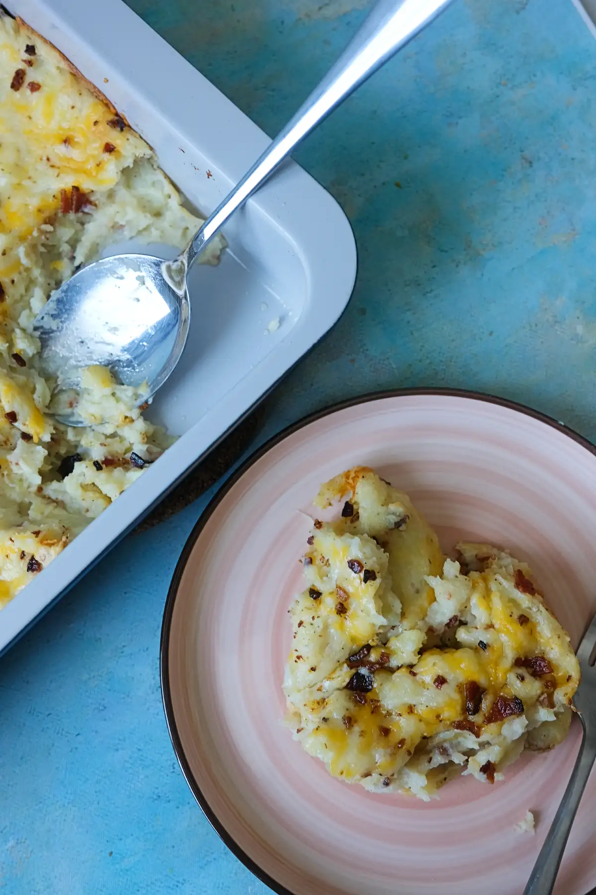 Spoon scooping loaded baked potato casserole from a baking dish onto a plate.