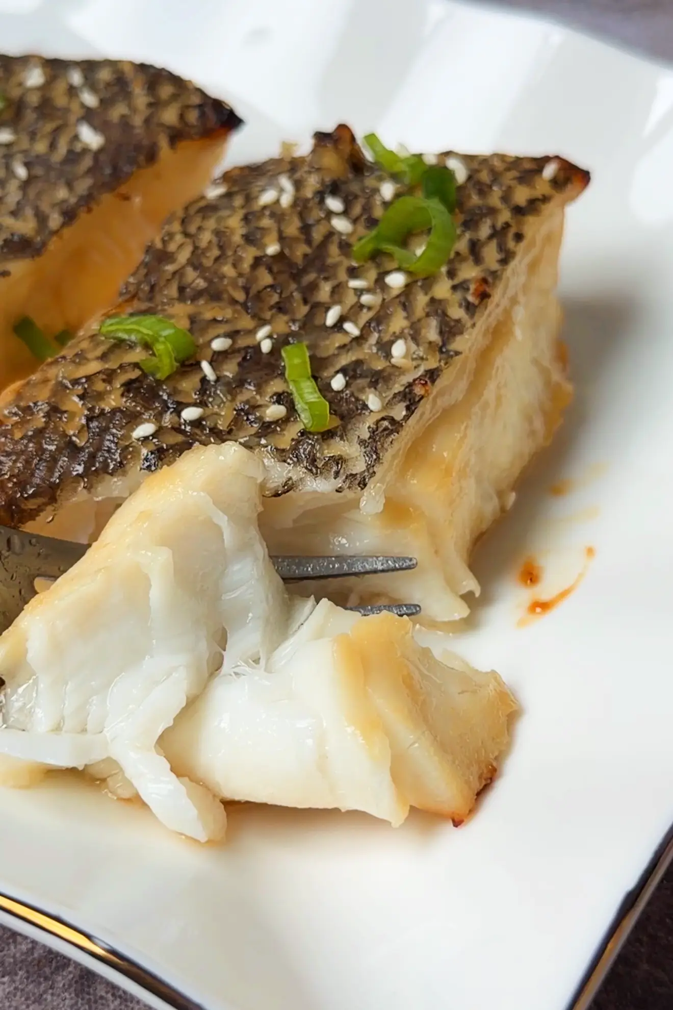 Fork holding a flaky piece of miso glazed Chilean sea bass