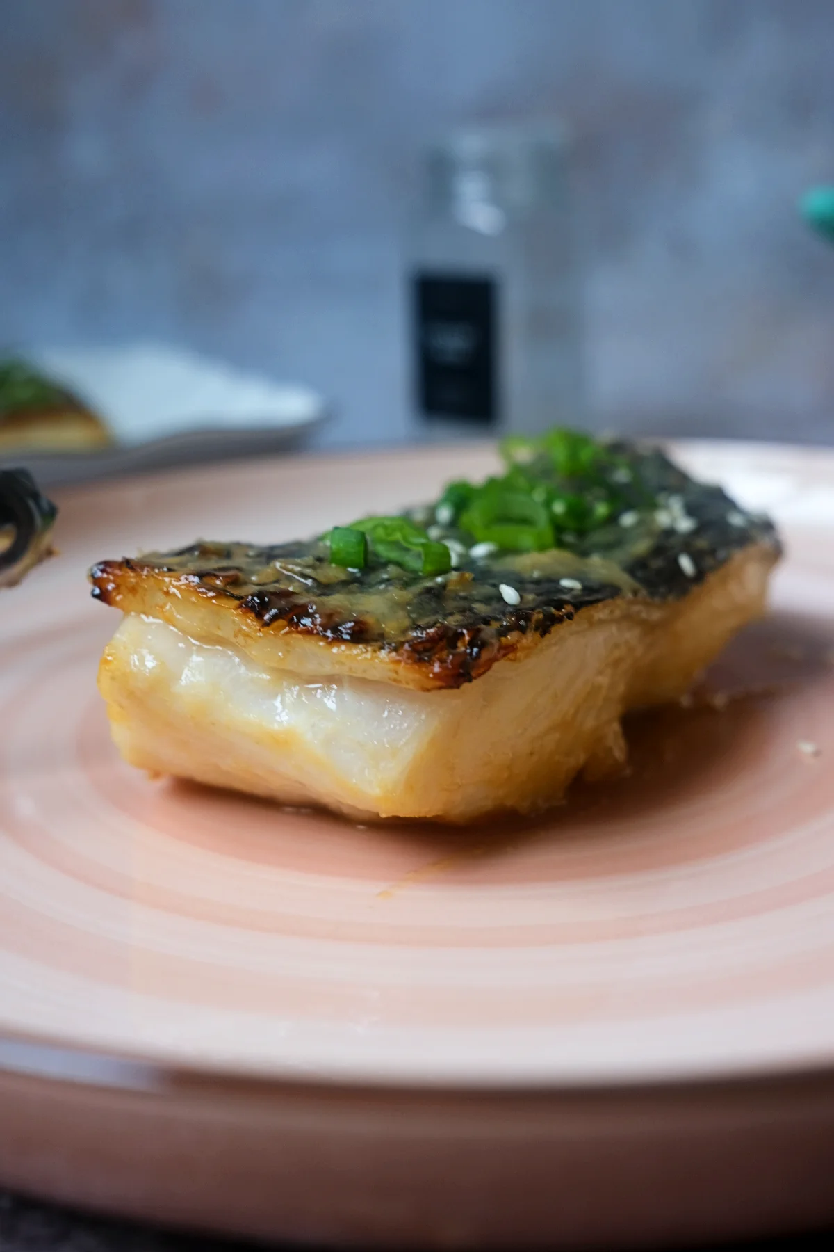 Miso glazed Chilean sea bass with crispy skin on a pink plate