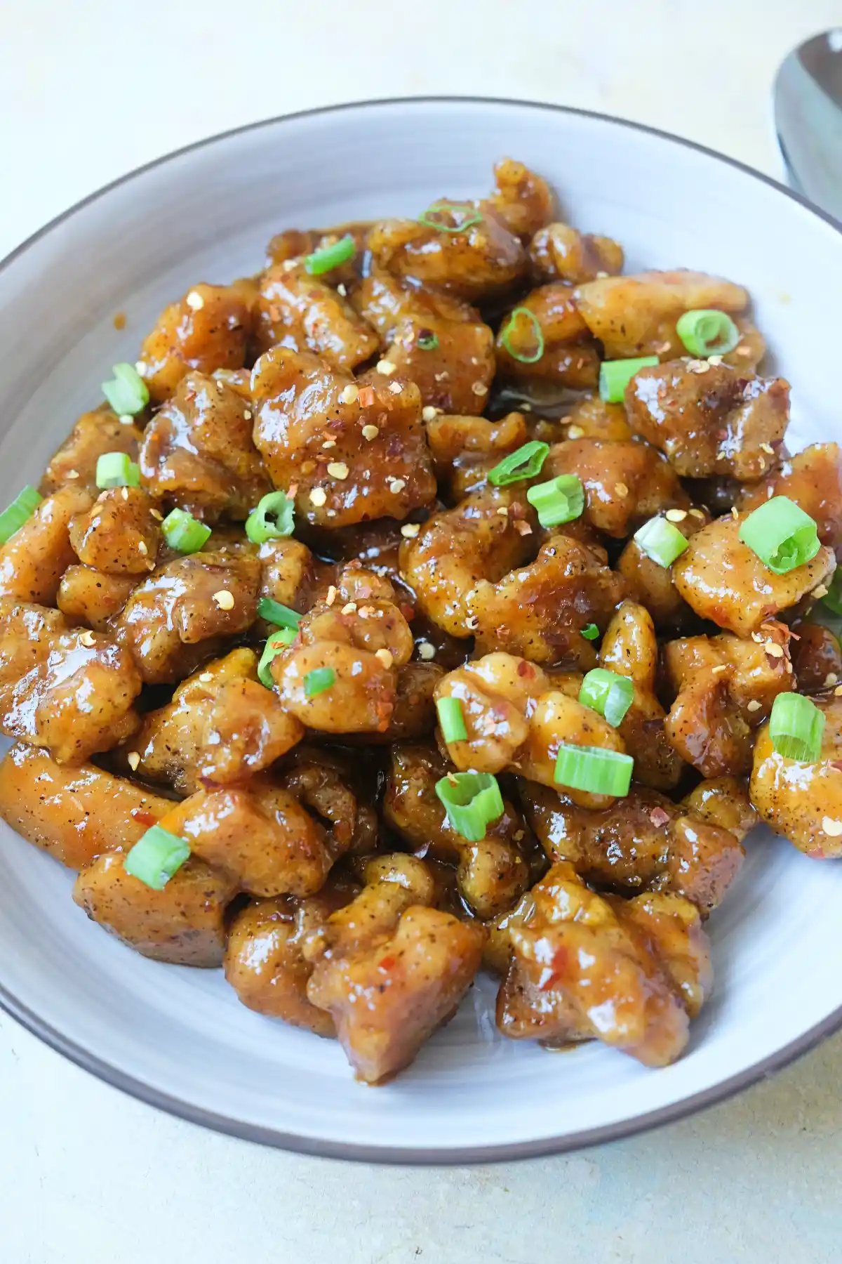 Hot Orange Chicken in a bowl garnished with green onions and chili flakes.