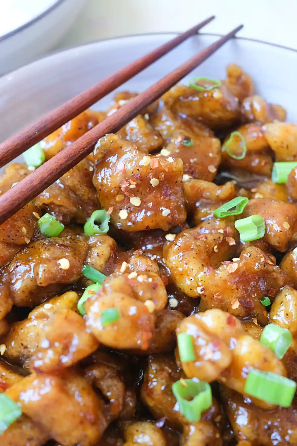 Close-up of spicy orange chicken coated in a glossy orange sauce with chili flakes and green onions.