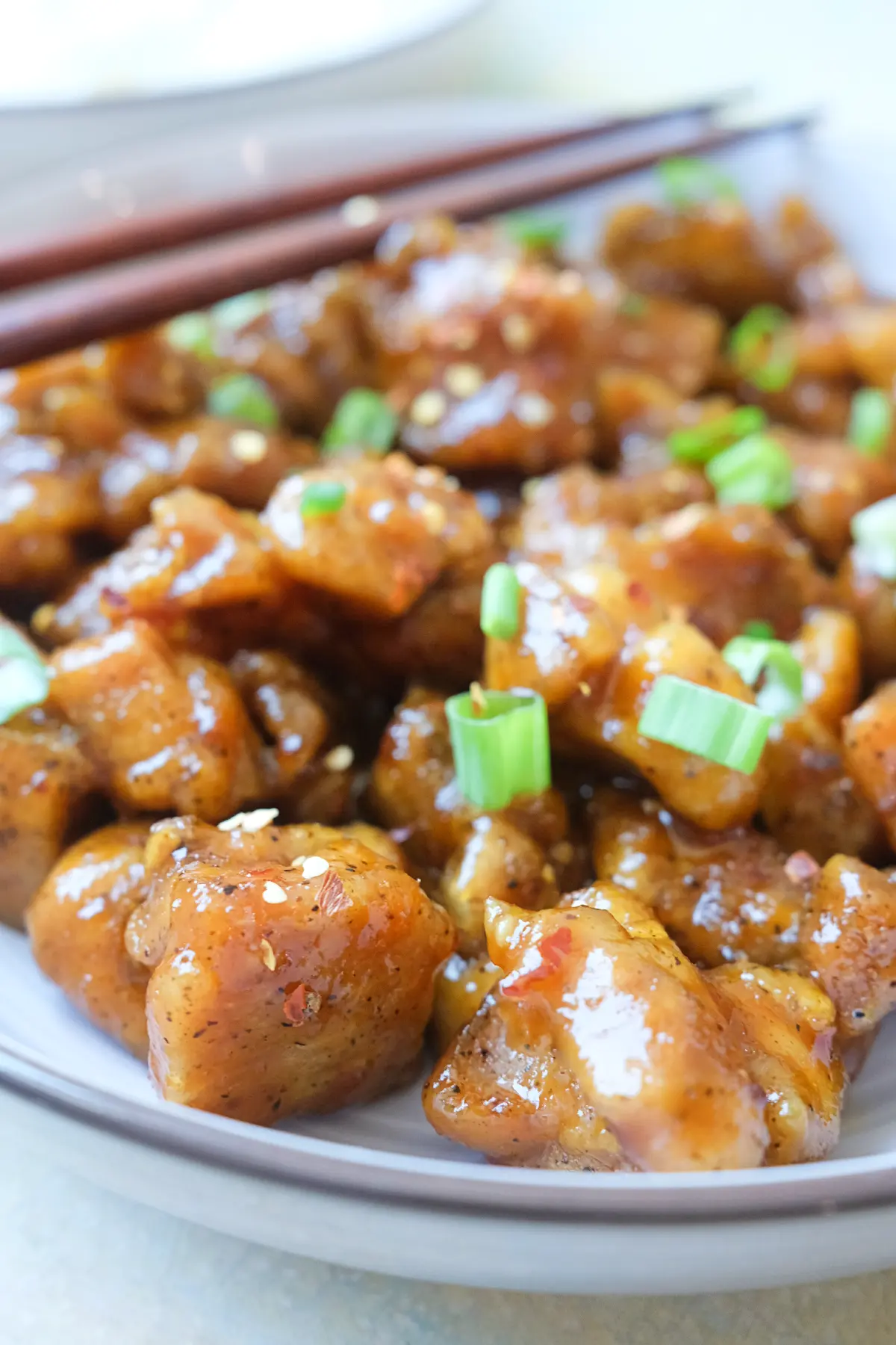 Sticky spicy orange chicken with a sweet citrus glaze served with chopsticks.