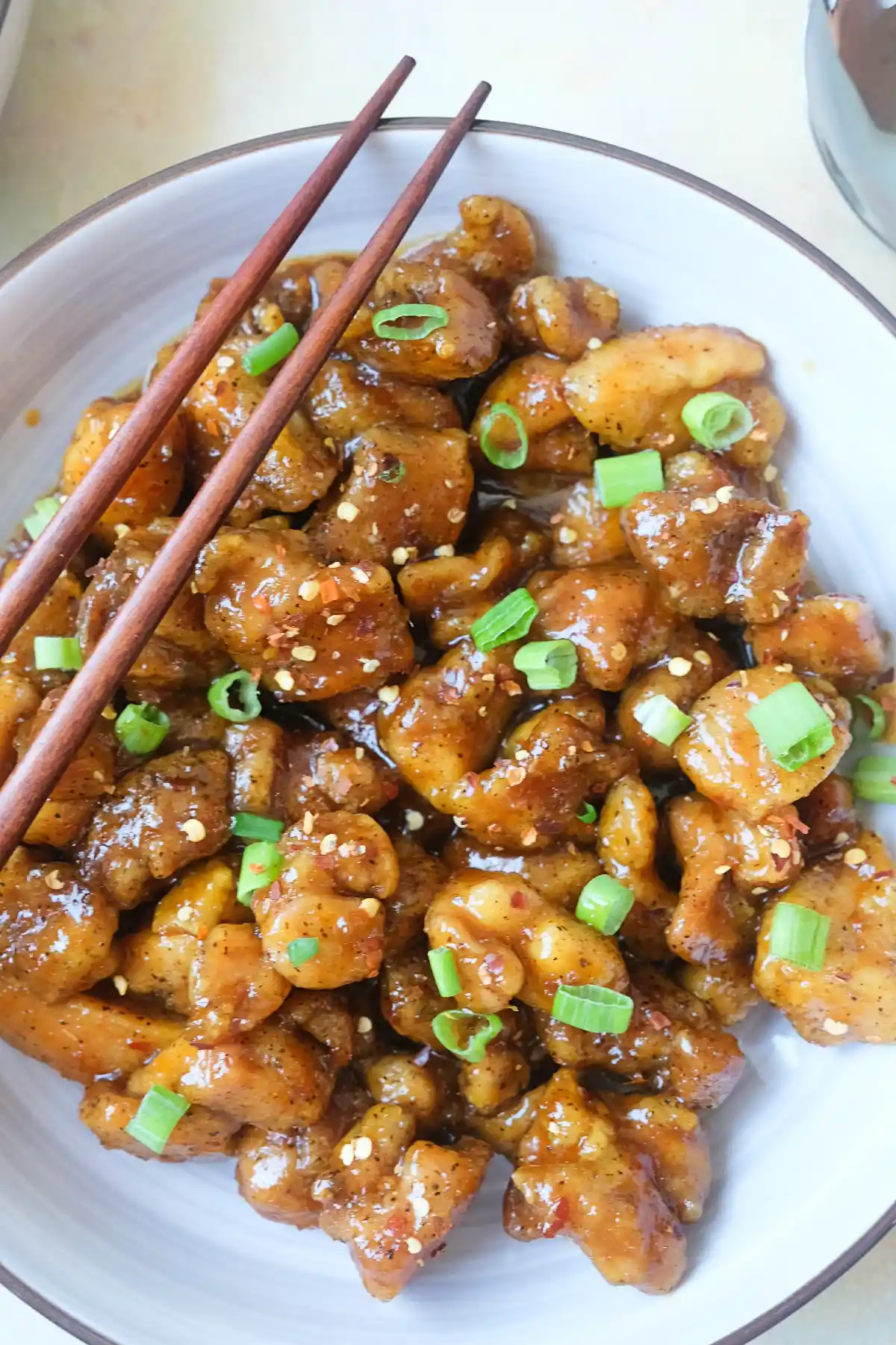 Close-up of spicy orange chicken coated in a glossy orange sauce with chili flakes and green onions.
