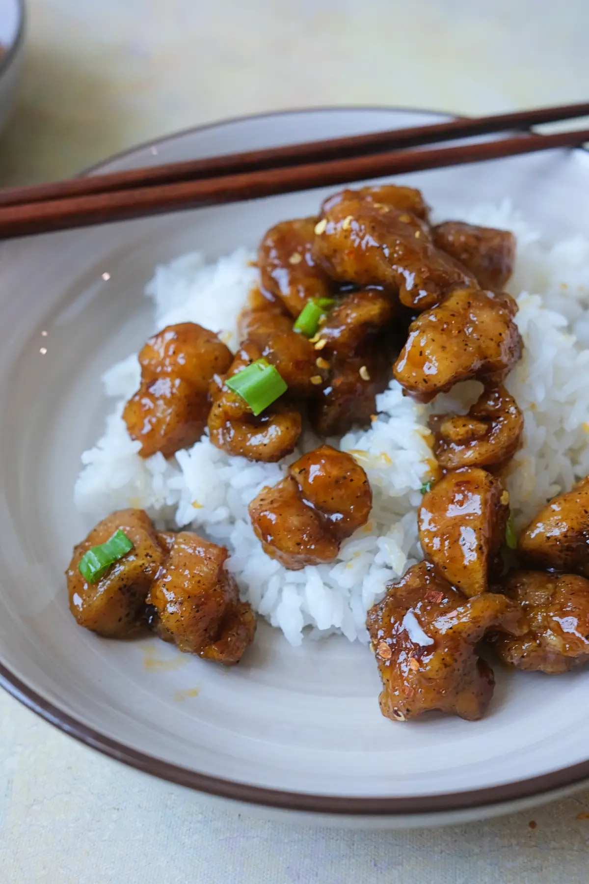 Spicy orange chicken and rice bowls topped with green onions and chili flakes.