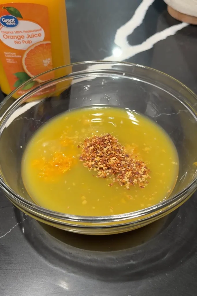 Mixing orange juice, orange zest, and red pepper flakes in a bowl to make spicy orange chicken sauce.