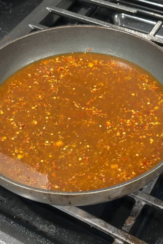 Pouring the homemade spicy orange sauce into the skillet to begin cooking.