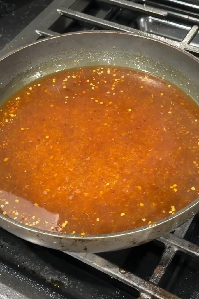 Simmering the orange sauce until it starts to thicken and reduce.