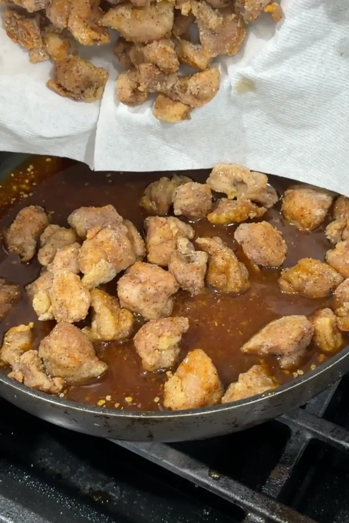 Adding the cooked chicken back to the skillet with the thickened orange sauce.
