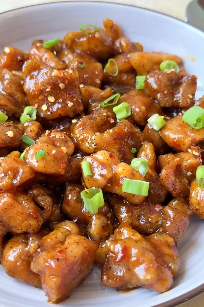 Close-up of homemade hot orange chicken garnished with green onions and red pepper flakes.
