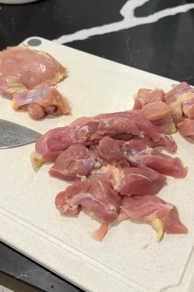 Cutting boneless chicken thighs into bite-sized pieces on a cutting board for orange chicken.