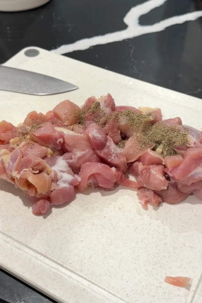 Seasoning chicken thigh pieces with salt and black pepper before coating.