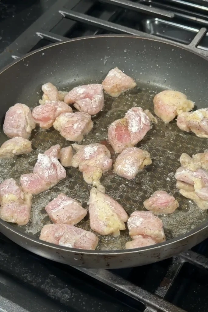 Cooking flour-coated chicken pieces in a skillet with oil until lightly browned.