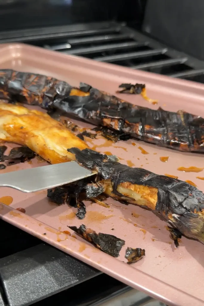 Peeling the charred skin from a freshly roasted eggplant while keeping the stem attached.