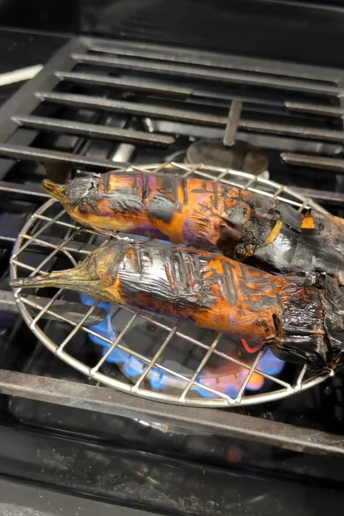 Charred roasted eggplants on a wire rack over an open flame.